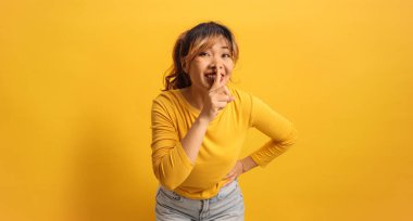 Neşeli genç Asyalı kadın sarı bir arka plana karşı sessiz hareketler yapıyor.