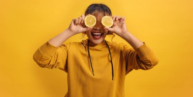 Sarı arka planda limon tutan neşeli Asyalı bir kadın.