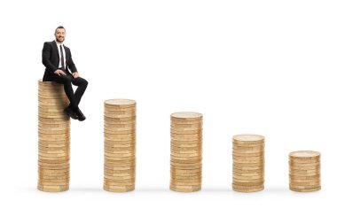 Beyaz arka planda izole edilmiş en yüksek madeni para yığınının üzerinde oturan işadamı