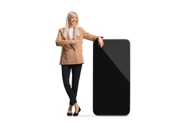 Uzun boylu bir kadın beyaz arka planda izole edilmiş büyük bir cep telefonunu işaret ediyor.
