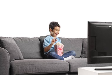 Bir kutu patlamış mısırla kanepede oturan ve televizyon izleyen bir çocuk.