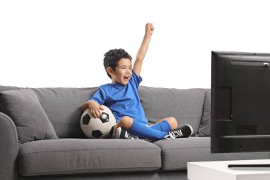 Kanepede oturan, elinde futbol topu olan ve beyaz arka planda izole bir şekilde tezahürat yapan bir çocuk.