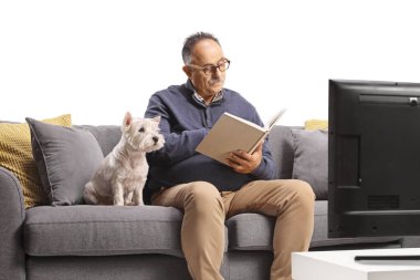 Kanepede oturan ve beyaz arka planda izole bir kitap okuyan olgun bir adam.