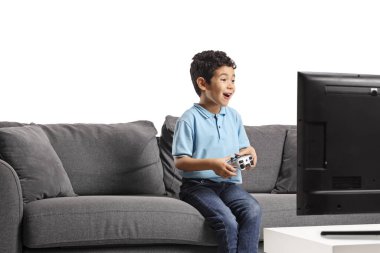 Kanepede oturup beyaz arka planda izole edilmiş video oyunları oynayan heyecanlı Asyalı çocuk.