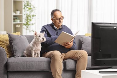 Kanepede oturmuş kitap okuyan, batılı bir teriyer köpeği olan olgun bir adam. 