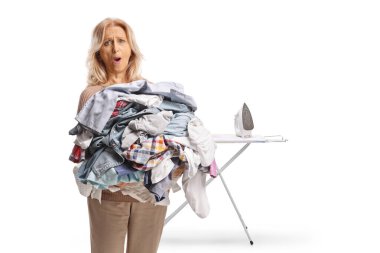 Kızgın kadın beyaz arka planda büyük bir ütü elbisesi yığını tutuyor.