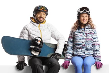 Genç bir adam ve kadın boş bir panelde oturuyor ve beyaz arka planda izole edilmiş bir snowboard tutuyor.
