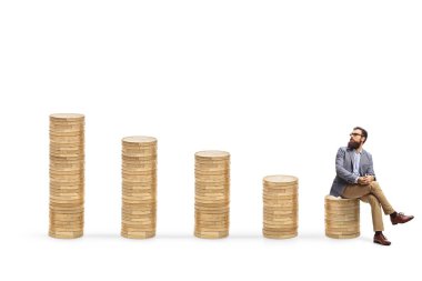 Bozuk paraların üzerinde oturan ve beyaz arka planda izole edilmiş en yüksek yığına bakan adam.