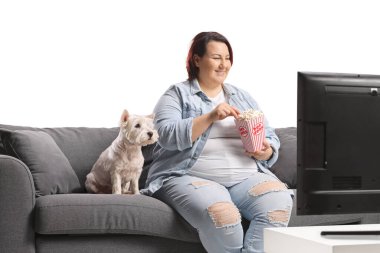 Kanepede oturmuş bir köpekle patlamış mısır yiyen ve televizyon izleyen şişman bir kadın.