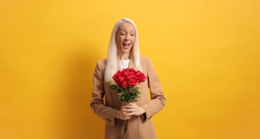 Sarı arka planda kırmızı güller tutan bir kadın. 