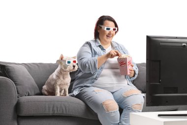 Elinde bir kutu patlamış mısırla kanepeye oturmuş köpeğiyle 3D film izleyen şişman bir kadın.