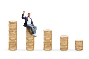 Gülümseyen genç adam bozuk para yığınının üzerinde oturuyor ve beyaz arka planda izole edilmiş kameraya el sallıyor.