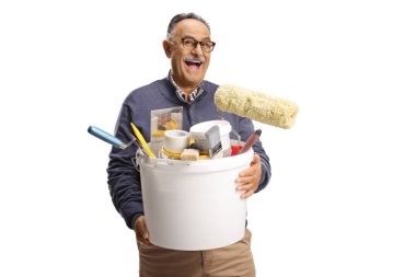 Neşeli olgun bir adam elinde kovayla beyaz arka planda izole edilmiş boya malzemeleri tutuyor.