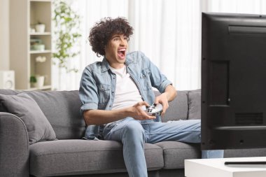 Kanepede oturup evde video oyunu oynayan heyecanlı adam.