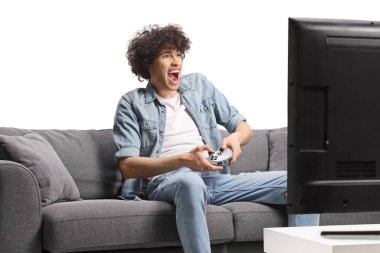 Kanepede oturup beyaz arka planda izole edilmiş video oyunları oynayan heyecanlı genç adam.