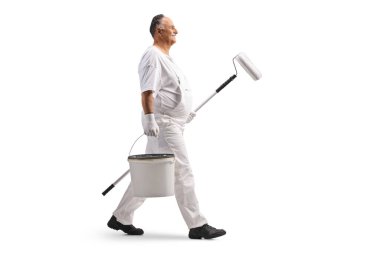 Olgun bir erkek ressam beyaz arka planda bir kova ve bir boya silindiri ile yürüyor.