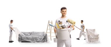 Boyacı elinde fırçalarla bir kova tutuyor ve beyaz arka planda izole edilmiş mobilyaları koruyor.