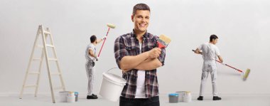 Fırçalı ve renkli kovalı bir adam boyacıların önünde duvar boyuyor.