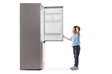 Şaşırmış bir çocuğun beyaz arka planda izole edilmiş boş bir buzdolabını açarken tam boy profil çekimi.