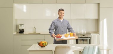 Pijamalı genç adam mutfakta kahvaltı tepsisi tutuyor.