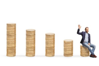 Beyaz arka planda izole edilmiş kameraya el sallayan para yığınları üzerinde genç profesyonel bir adam.