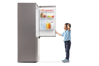 Şaşırmış bir çocuğun beyaz arka planda izole edilmiş bir buzdolabına bakarken tam boy profil fotoğrafı.