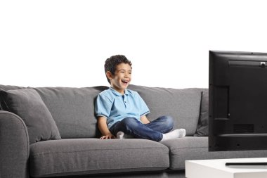 Çocuk kanepede oturup televizyon seyrediyor ve beyaz arka planda izole bir şekilde gülüyor.