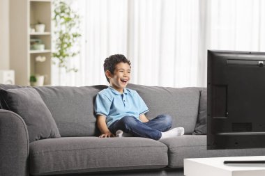 Çocuk kanepede oturmuş televizyon izliyor ve gülüyor.