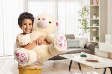 Mutlu çocuk evde oyuncak ayıya sarılıyor.