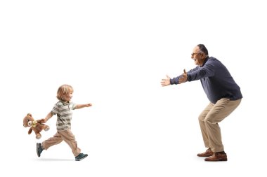 Beyaz arka planda izole edilmiş yetişkin bir adama sarılmak için koşan oyuncak ayılı bir çocuk.