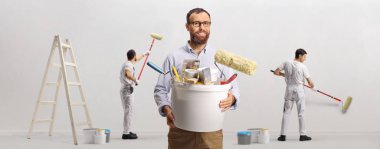 Bir duvar boyayan ev ressamları takımı ve beyaz arka planda izole edilmiş fırçalı kova tutan adam.