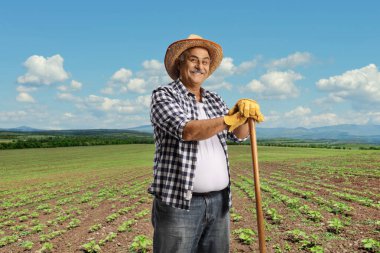 Mature farmer with a straw hat leaning on a wooden stick on a field