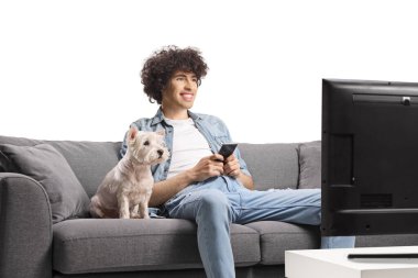 Kanepenin önünde oturan ve beyaz arka planda izole edilmiş akıllı telefonu tutan köpekli genç bir adam.