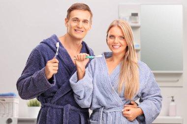Banyoda diş fırçası tutan genç bir çift. 