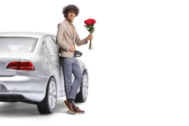 Genç adam arabaya yaslanıyor ve beyaz arka planda bir demet kırmızı gül tutuyor.