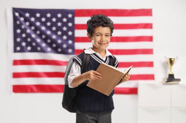 Çocuk Amerikan bayrağının önünde durmuş kitap okuyor.