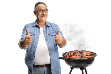 Sıradan, olgun, gülümseyen bir adam beyaz arka planda izole edilmiş bir bbq 'ın önünde iki parmağını da gösteriyor.