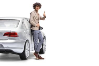 Genç adam arabaya yaslanıyor ve beyaz arka planda izole bir şekilde işaret veriyor.