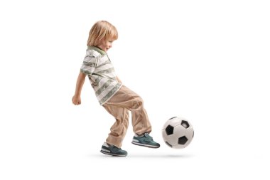 Küçük sarışın çocuk beyaz arka planda topu tekmeliyor.