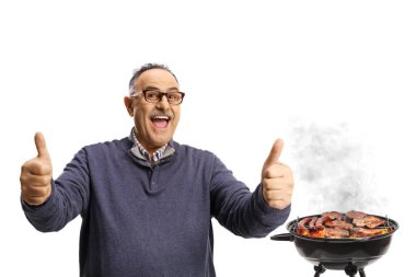 Olgun bir adam beyaz arka planda izole edilmiş bir barbekü önünde baş parmak işareti yapıyor.