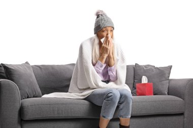 Battaniyeye sarılı bir kadın kanepeye oturur ve beyaz arka planda izole bir şekilde burnunu temizler.