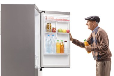 Beyaz arka planda izole edilmiş buzdolabının önünde meyve suyu şişesi tutan yaşlı bir adam.