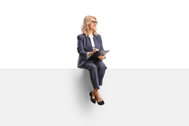 Orta yaşlı bir kadın boş bir panelde oturuyor ve beyaz arka planda izole edilmiş bir panoya yazı yazıyor.