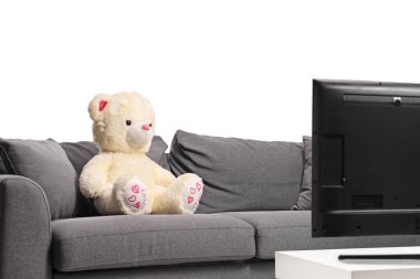 Beyaz ayıcık beyaz arka planda izole edilmiş gri bir televizyonun önündeki gri koltukta.