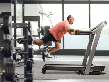 Spor salonundaki koşu bandından düşen olgun bir adam.