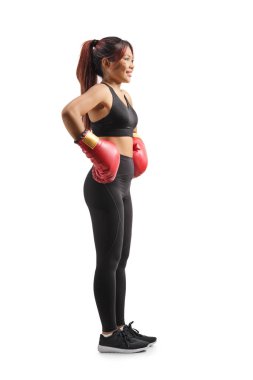 Beyaz arka planda kırmızı boks eldiveni giyen Asyalı genç bir kadının tam boy profil fotoğrafı.