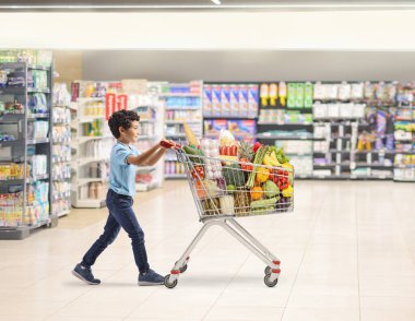 Markette elinde gıda ürünleriyle dolaşan bir çocuğun tam boy profil fotoğrafı. 