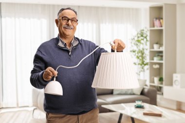 Cheerful mature man holding a white pendant lamp in a living room
