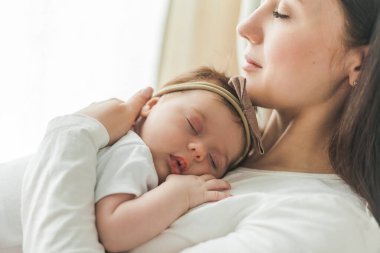 Genç bir annenin kollarında beyaz takım elbiseli, tatlı, siyah saçlı, yeni doğmuş bir kızın yakın portresi. Annelik. Ebeveyn. İyi uykular. Ev.