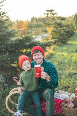 Genç ve güzel bir aile markette bir Noel ağacı seçiyor. Ebeveynler ve küçük çocuklar için şenlikli kış tatili. Çayı doğada iç..